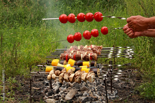 Cooking kebabs and tomatoes on skewers outdoors.