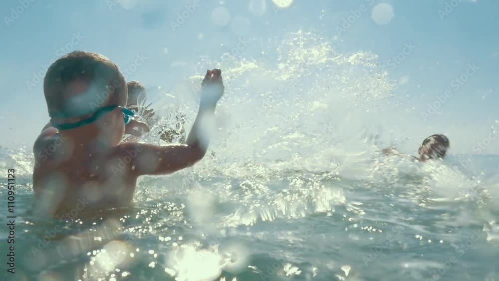 Slow motion shot of united parents and child playing in the sea splashing water.