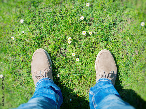 Summer is coming! Male boots on the grass with first flowers. Top view.