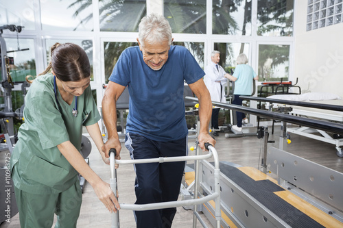Nurse Assisting Senior Man To Walk Using Walker