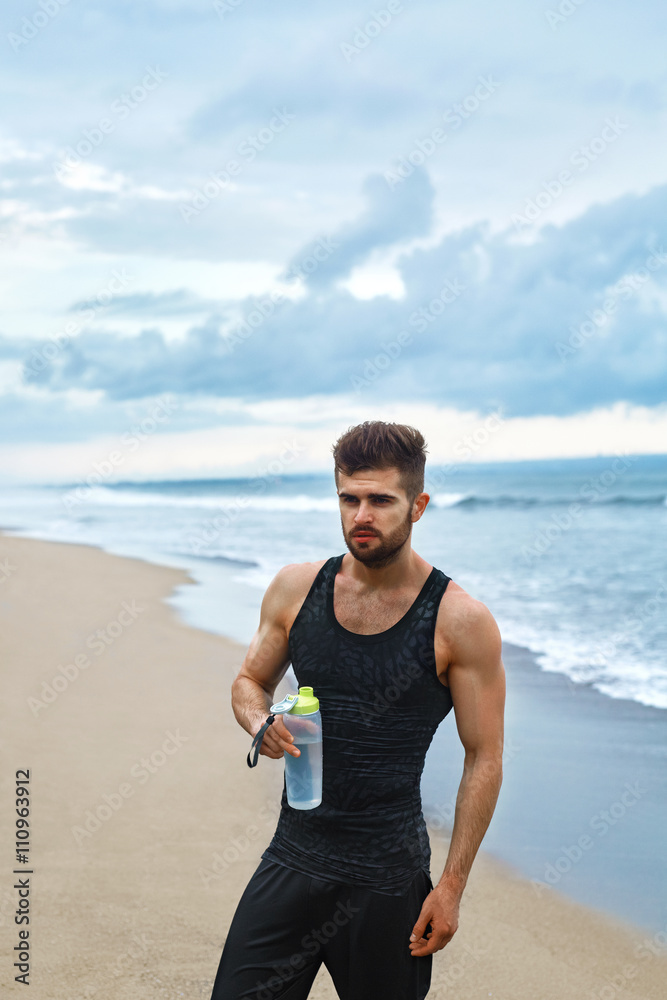 Portrait Of Healthy Athletic Man With Fit Body Holding Bottle Of Refreshing Water, Resting After Workout Or Running At Beach. Thirsty Male With A Drink After Outdoor Training. Sports, Fitness Concept Portrait Of Healthy Athletic Man With Fit Body Holding Bottle Of Refreshing Water, Resting After Workout Or Running At Beach. Thirsty Male With A Drink After Outdoor Training. Sports, Fitness Concept