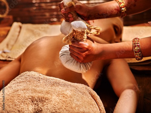 Woman having ayurvedic massage with back pouch of rice. Close up of exotic India massage.