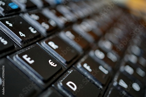 Detail of a black dusty laptop keyboard with a focus on a sign of Euro currency 