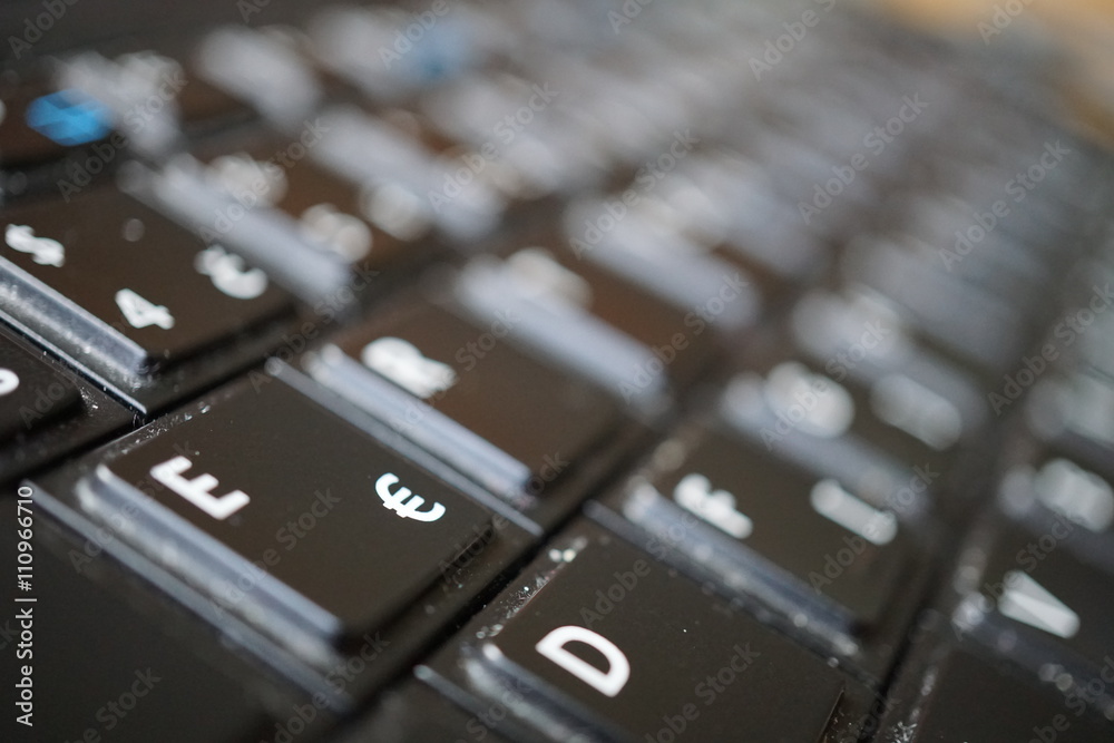 Detail of a black dusty laptop keyboard with a focus on a sign of Euro currency 