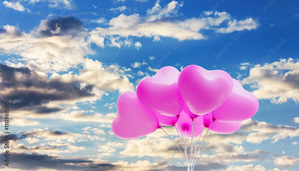 Group of lovely pink heart pattern balloons on puffy cloudy blue sky