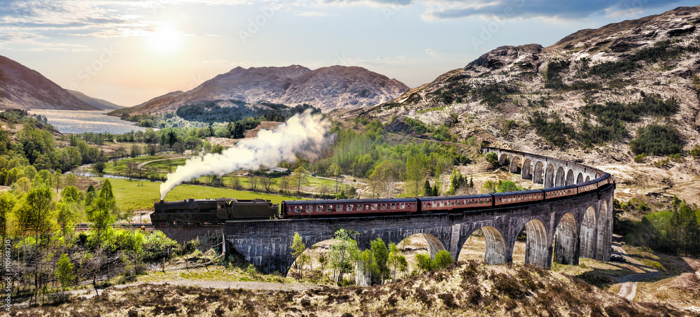 Fototapeta premium Wiadukt kolejowy Glenfinnan w Szkocji z pociągiem parowym Jacobite przeciwko zachód słońca nad jeziorem