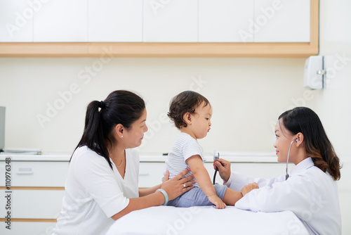 Young female pediatrician checking heartbeat of little baby