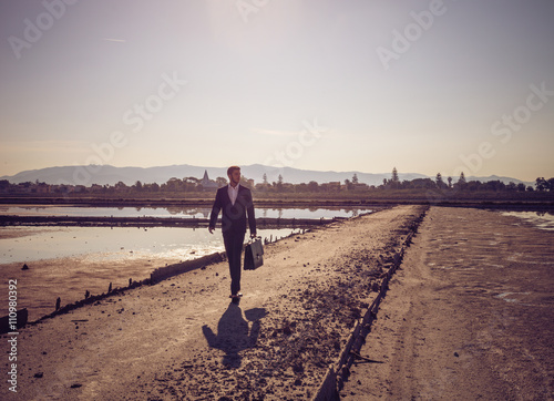 Mid adult businessman carrying briefcase walking along beach photo