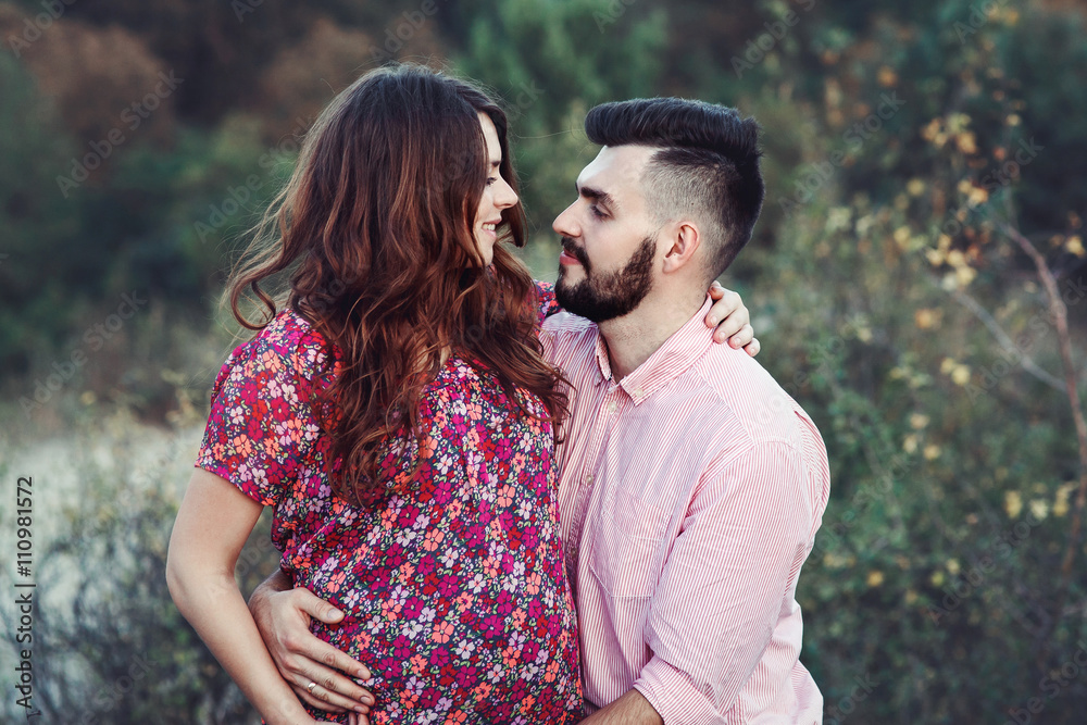 Happy handsome husband & beautiful pregnant wife kissing in natu Happy handsome husband & beautiful pregnant wife kissing in natu