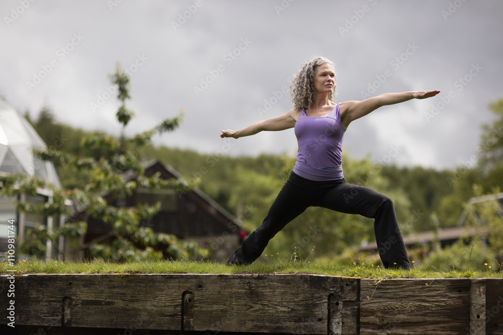 Mature woman practicing warrior pose in eco lodge garden Mature woman practicing warrior pose in eco lodge garden