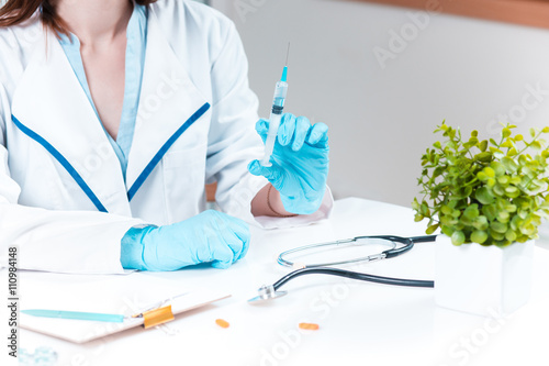 The hand in blue glove holding syringe against white medical gown 