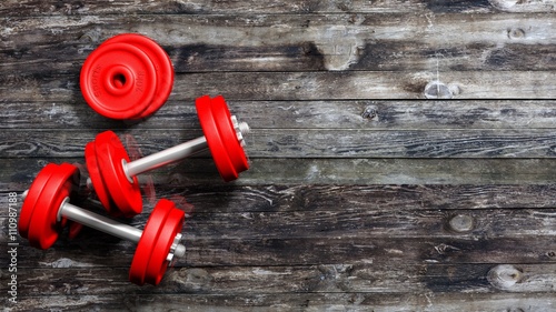 3D rendering of adjustable metallic red dumbbells, on wooden background with copy-space