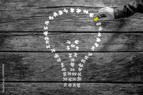 Photos Male hand placing the last missing  puzzle piece into a light bu