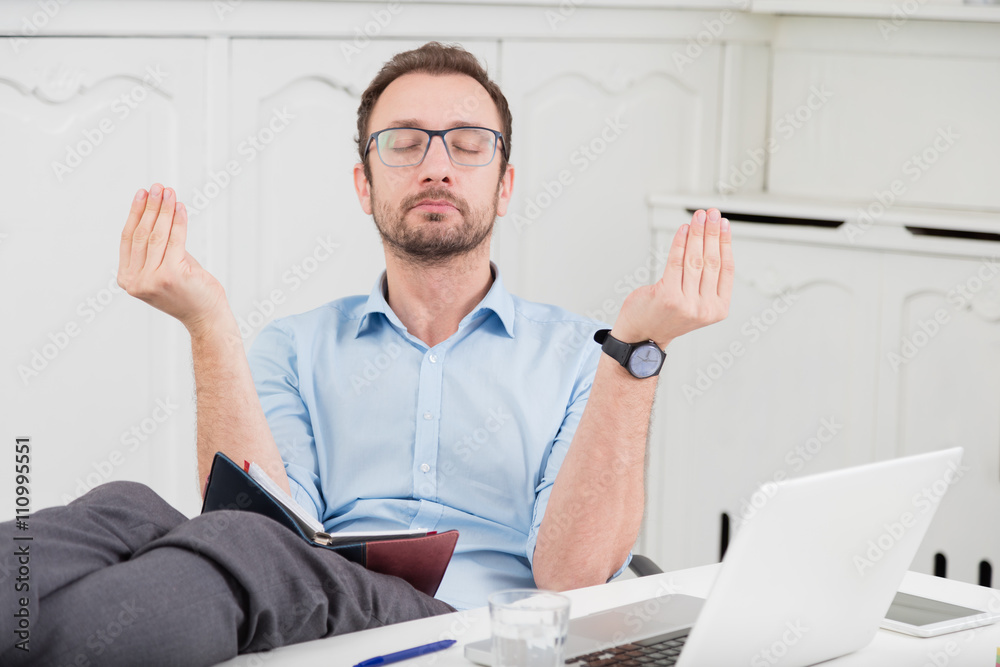 Businessman meditating in the office with his legs on the desk 
