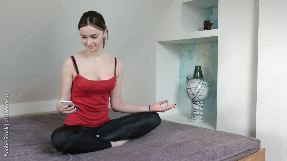 Teenage girl in red t-shirt sitting in lotus position on bed in attic bedroom and using smart phone Teenage girl in red t-shirt sitting in lotus position on bed in attic bedroom and using smart phone