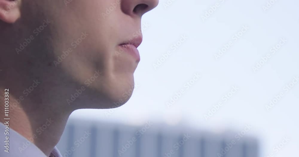 Big close up on smart young man in business suit smoking from a vaporizing pipe on urban streets. Slow motion recorded at 60fps.