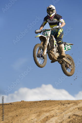 Young male motocross racer jumping muddy hill