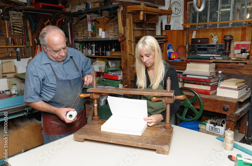 Senior man and young woman preparing to bind pages with thread in traditional bookbinding workshop photo