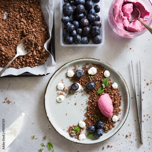 Mixed berry  mousse served on chocolate soil with cream drops, blueberries, lemon balm leaves and thyme flowers. Concept of food plating in modern nordic style.