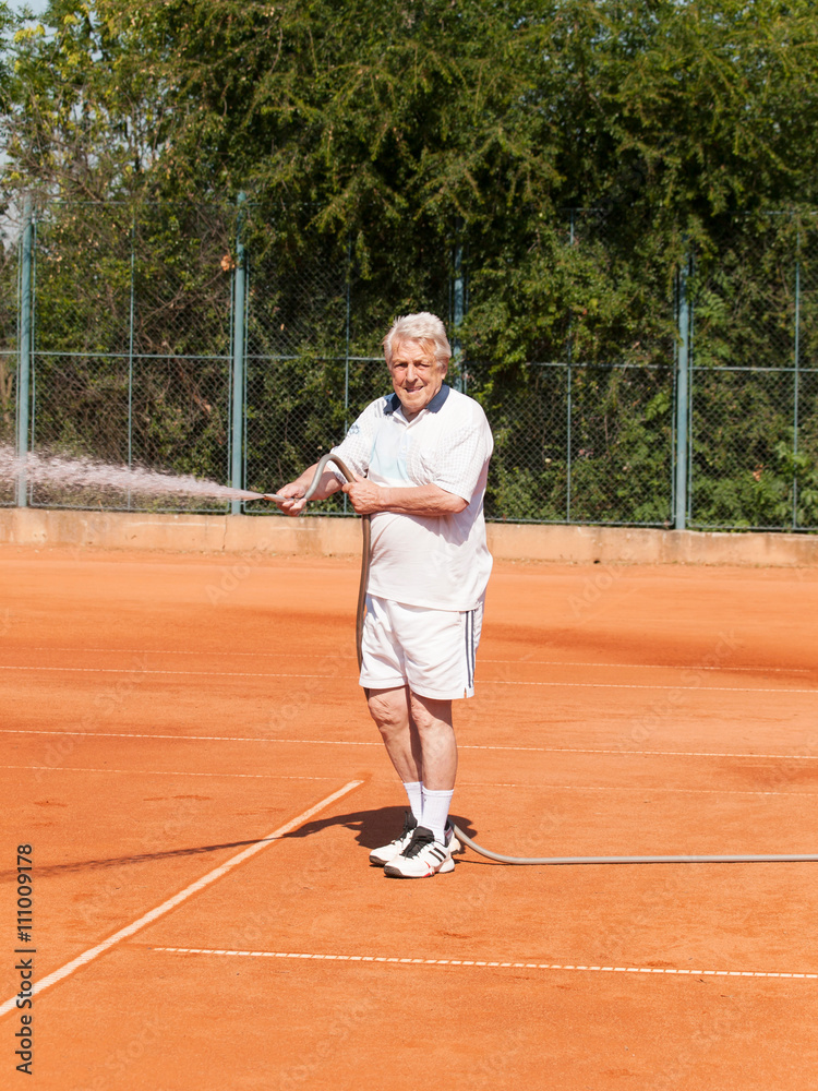 Senior men sprinklig tennis court before playing