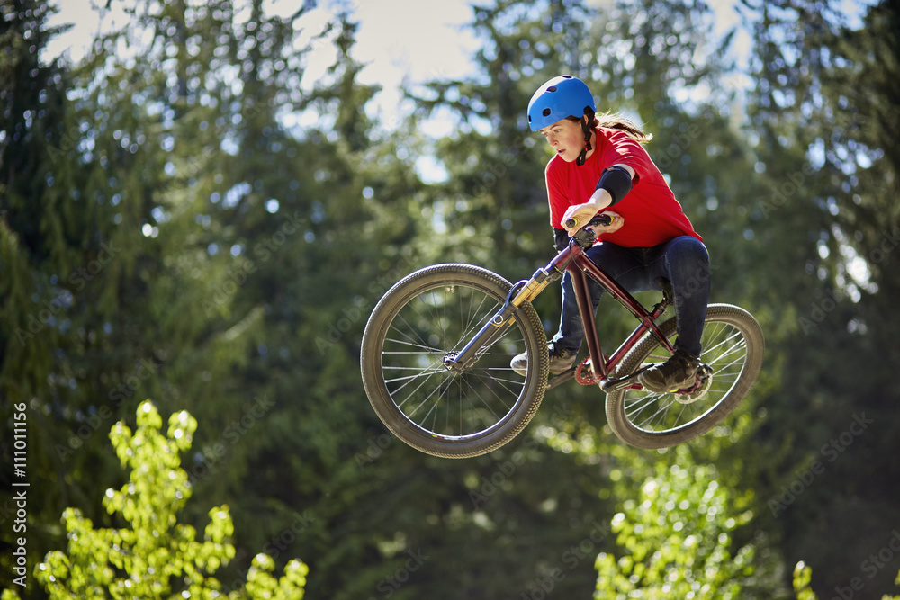 Young female bmx biker jumping mid air in forest Young female bmx biker jumping mid air in forest