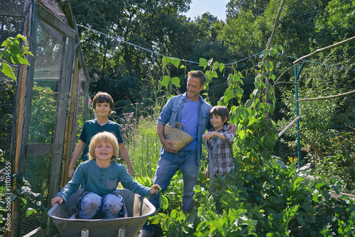 Man and three boys riding in wheelbarrow on allotment