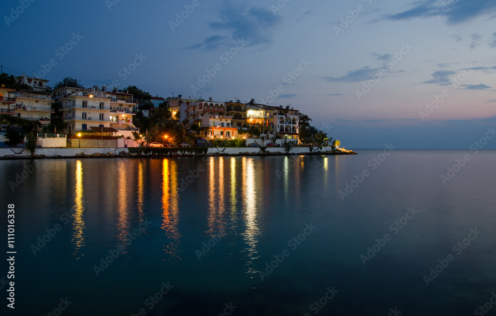 Greek island at dawn with calm peaceful relaxing sea water and reflections of lights on a beautiful night