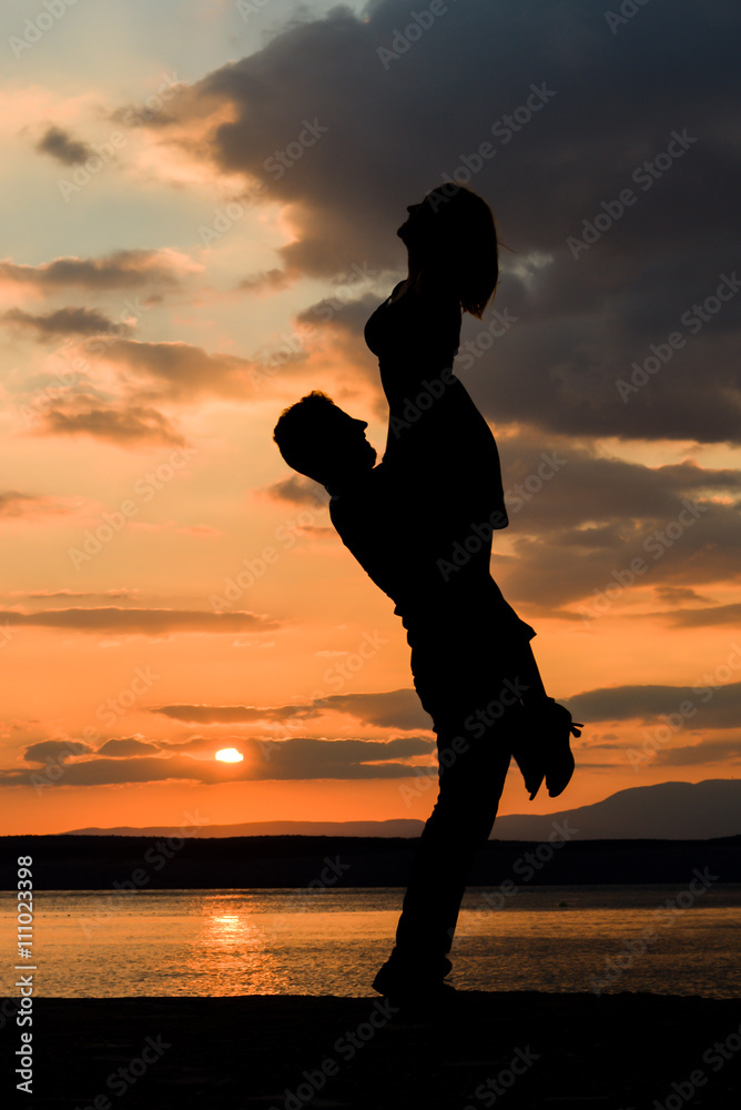 Lovers silhouettes at sunset holding each other, lifting