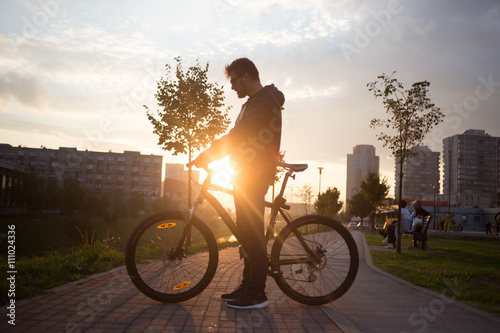Young handsome hipster man posing with bicycle on sunset