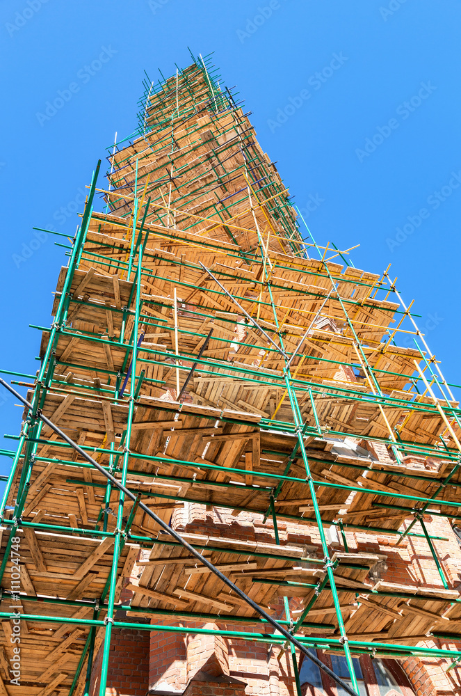 The spire of the Catholic Church in scaffolding against the blue