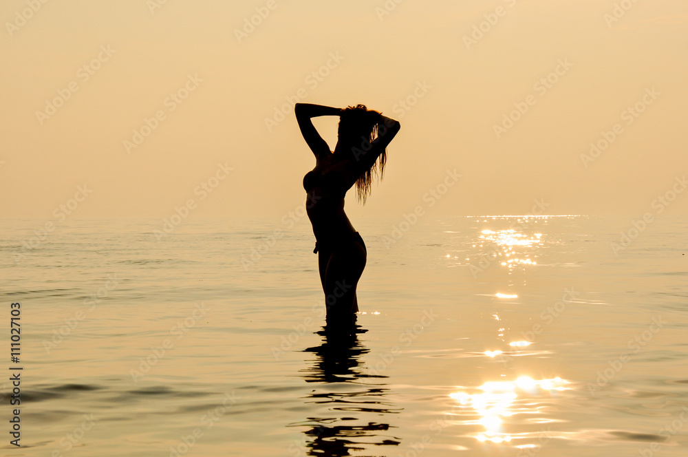 Girl silhouette at sunset in the water at seaside