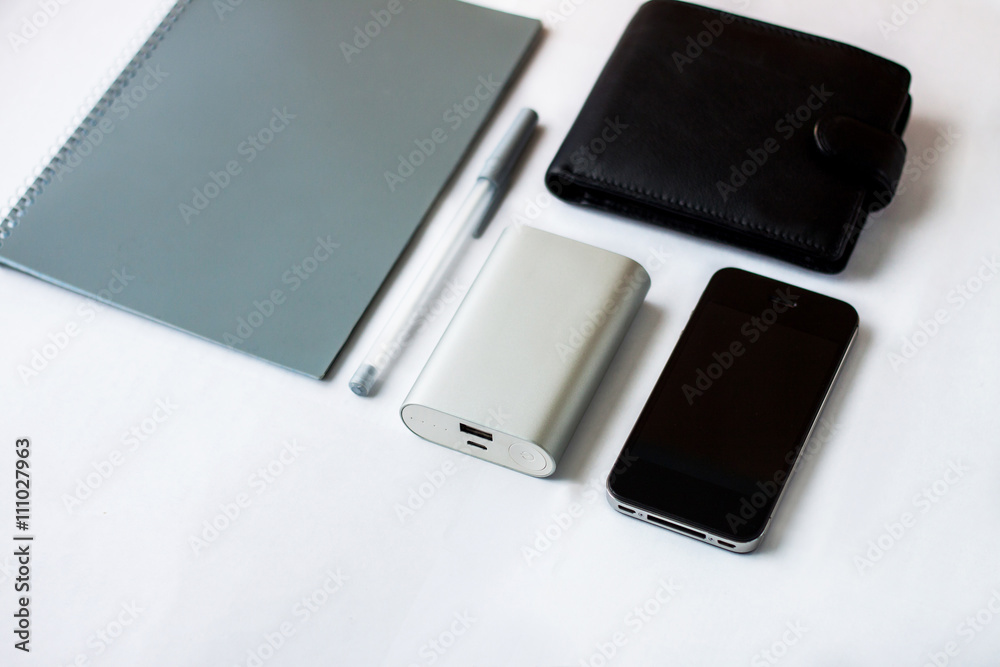 Equipment on a table (phone, portablecharger, purse, notebook, pen) Equipment on a table (phone, portablecharger, purse, notebook, pen)