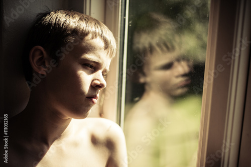 Sad shirtless child reflected in window photo