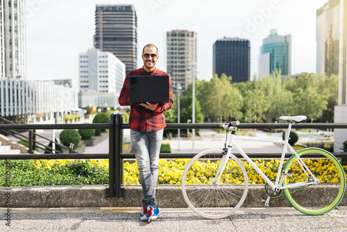 Young man with laptop and fixed gear bicycle in the city.