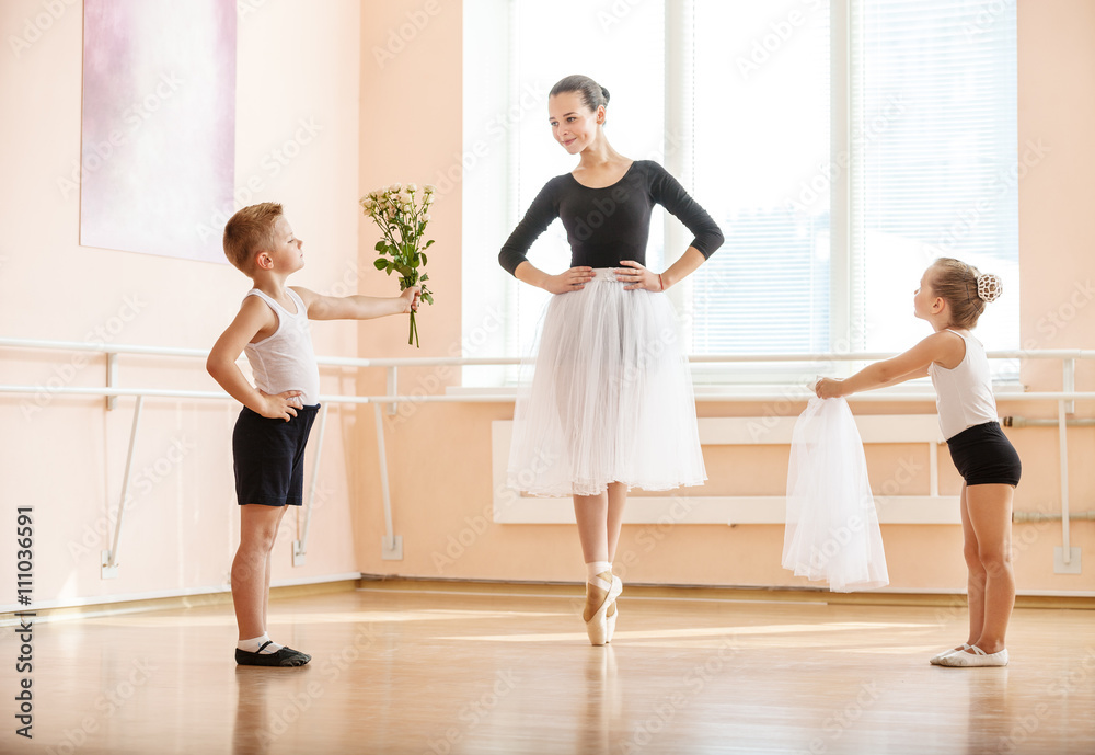 At ballet dancing class: young boy and girl giving flowers and veil to older student while she is dancing en pointe 