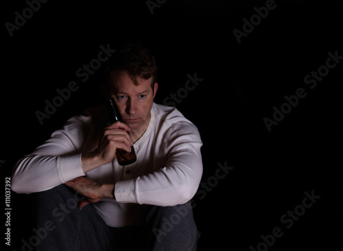 Mature man in thought while drinking beer in dark background © tab62