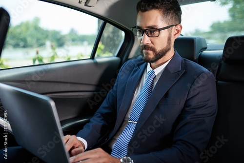 Concentrated businessman working on laptop when sitting on backseat of car © DragonImages