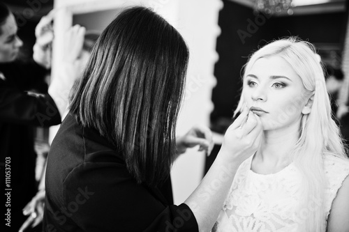 Young beautiful blonde bride applying wedding make up by makeup artist