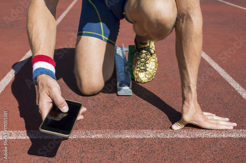 Athlete crouching at the starting line of a running track wearing USA colors wristbands checking his mobile phone