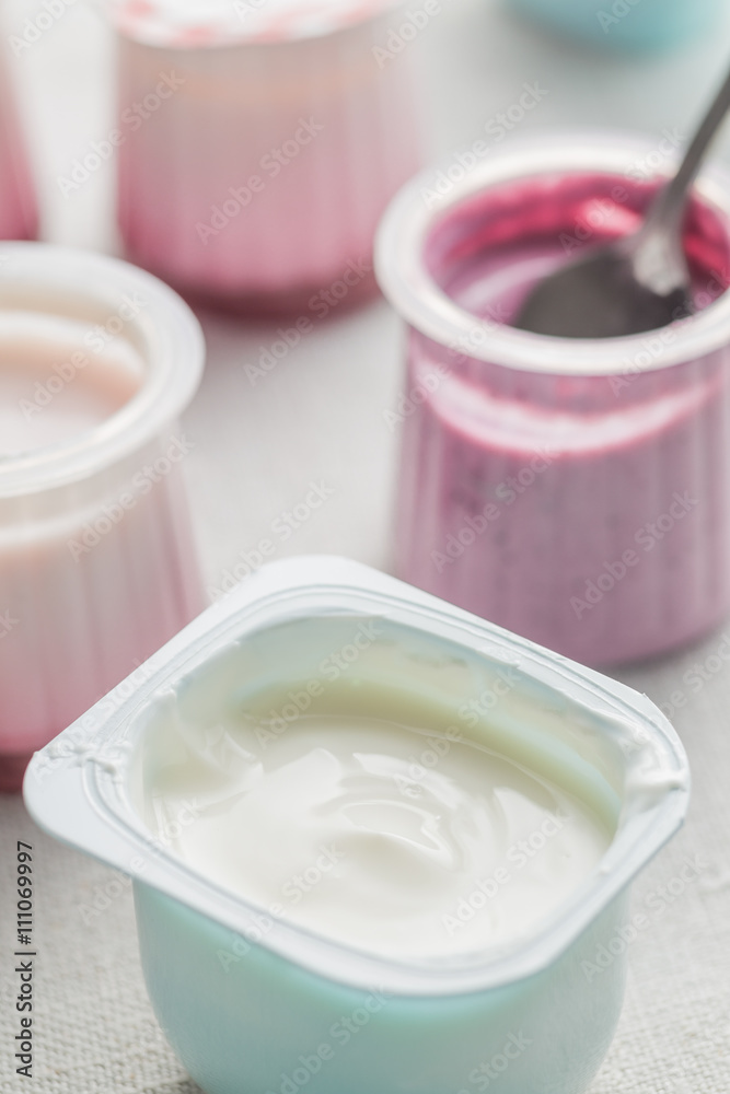 Yogurts assortment in plastic bowls on light cloth background. Natural and fruit healthy, diet, gourmet dessert for granola breakfast. Sweet yoghurts closeup. Yogurts assortment in plastic bowls on light cloth background. Natural and fruit healthy, diet, gourmet dessert for granola breakfast. Sweet yoghurts closeup.