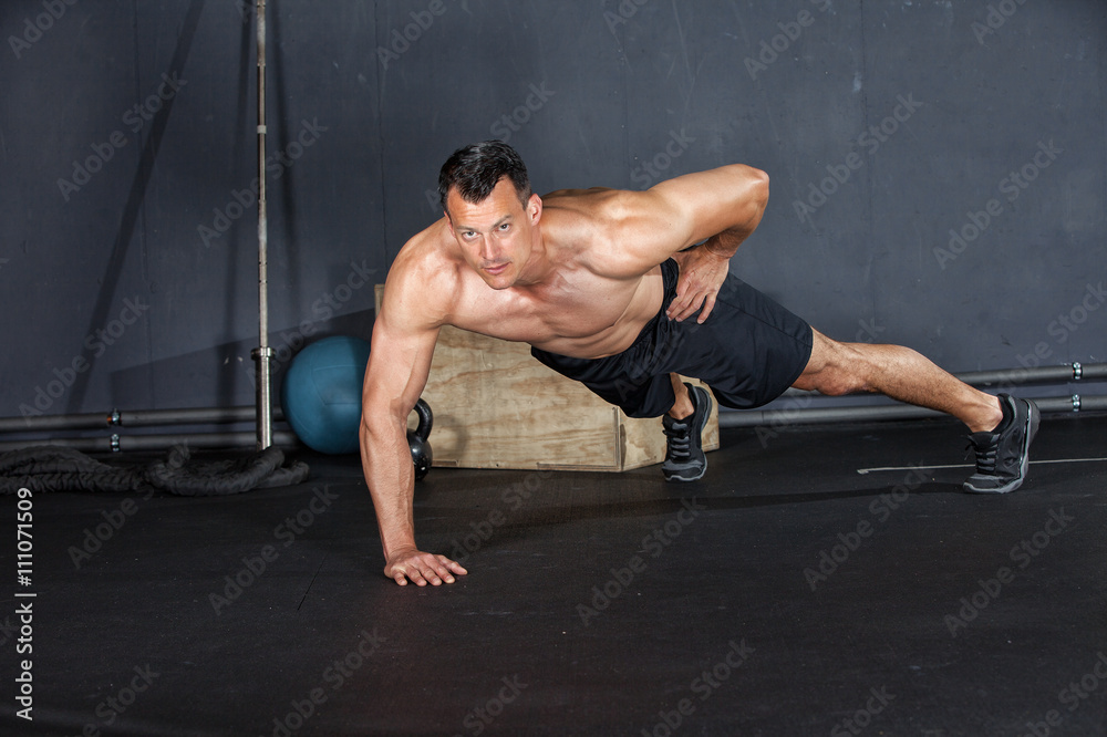 Fototapeta premium Man doing a push-up on one arm in a gym