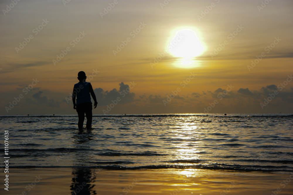 Silhouette of the asian boy standing at the beach during beautif