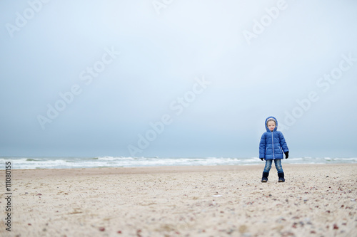 Adorable little girl playing by the ocean on winter day