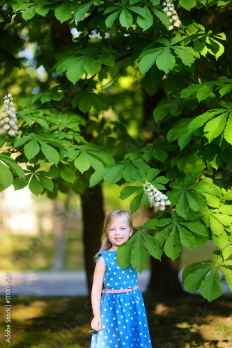 Adorable little girl by blossoming chestnut tree