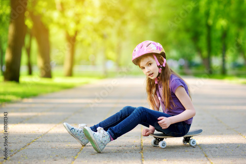 Cute little preteen girl wearing helmet sitting on a skateboard © MNStudio