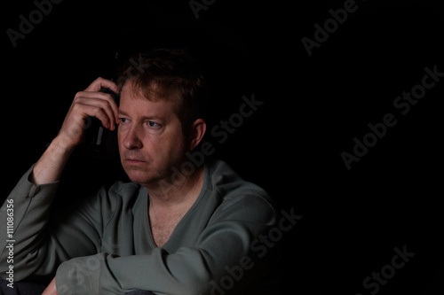 Mature man looking lost in thought while drinking beer in dark