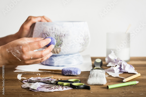 Decoupage hobbyist hands decorating a vase with lavender pattern - some artistic supplies on a table.  photo
