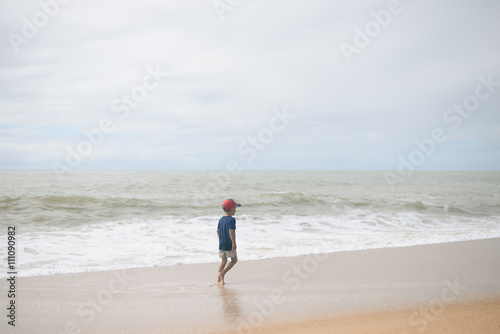 Back view of boy walking along the beach outside during sunset