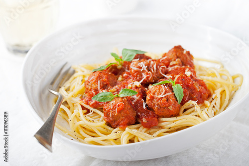 Meatballs in tomato sauce and fresh basil with spaghetti on a white plate