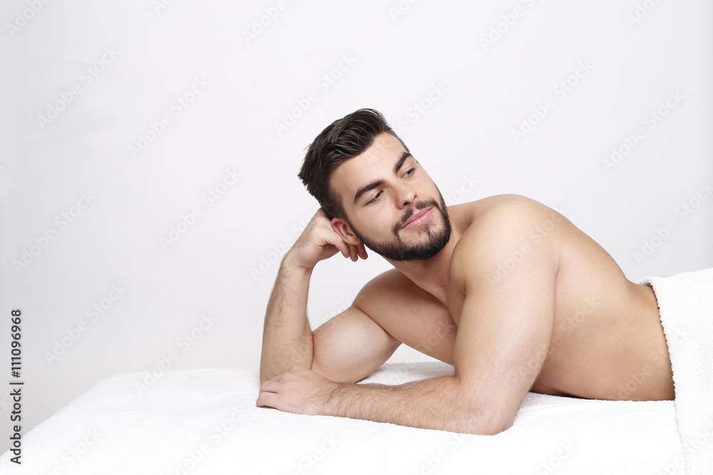Junger Bartträger liegt oben ohne auf Massageliege und schaut nach hinten Junger Bartträger liegt oben ohne auf Massageliege und schaut nach hinten